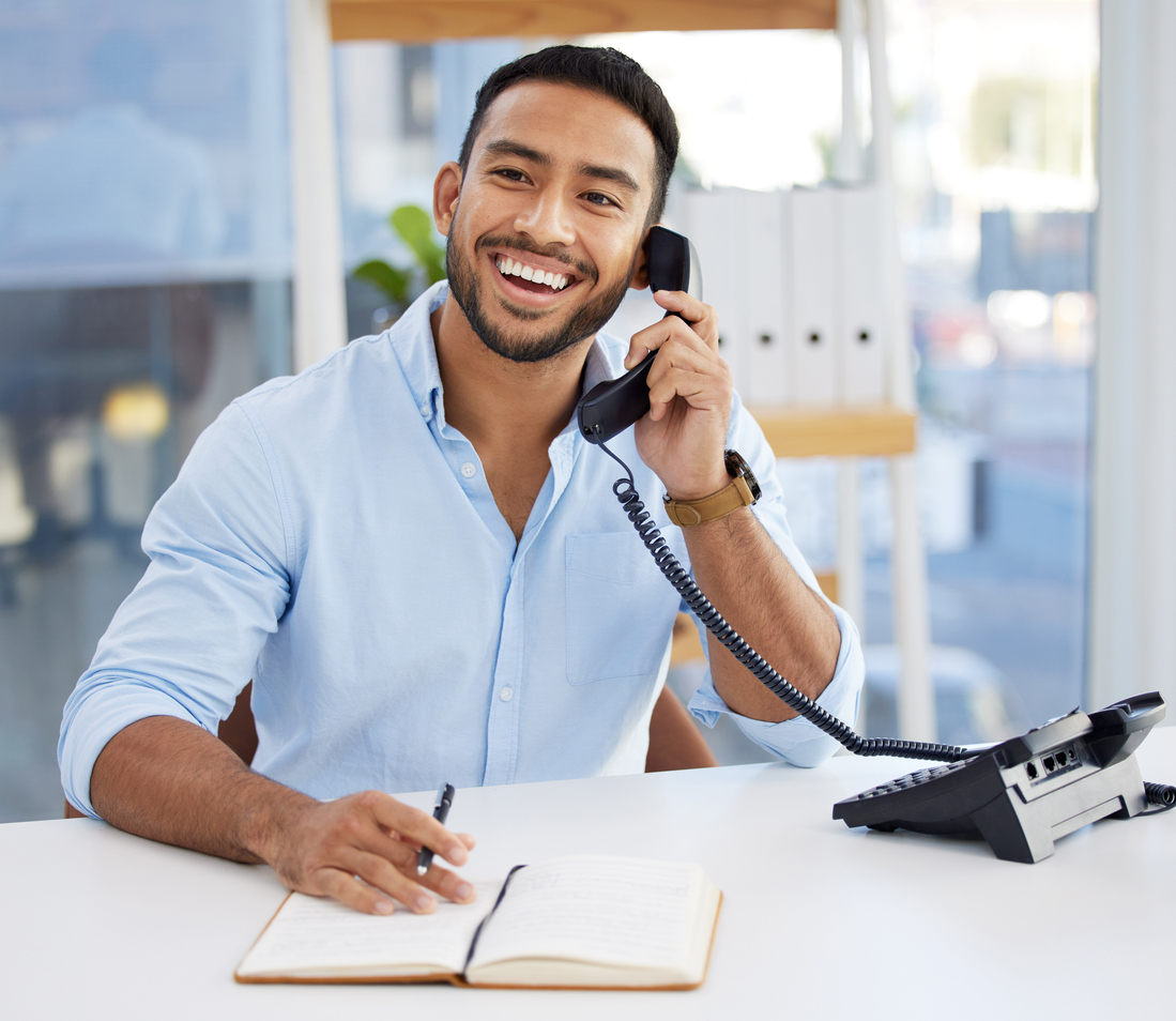 A person smiling while answering a phone call appearing cheerful and engaged as they hold the phone to their ear.