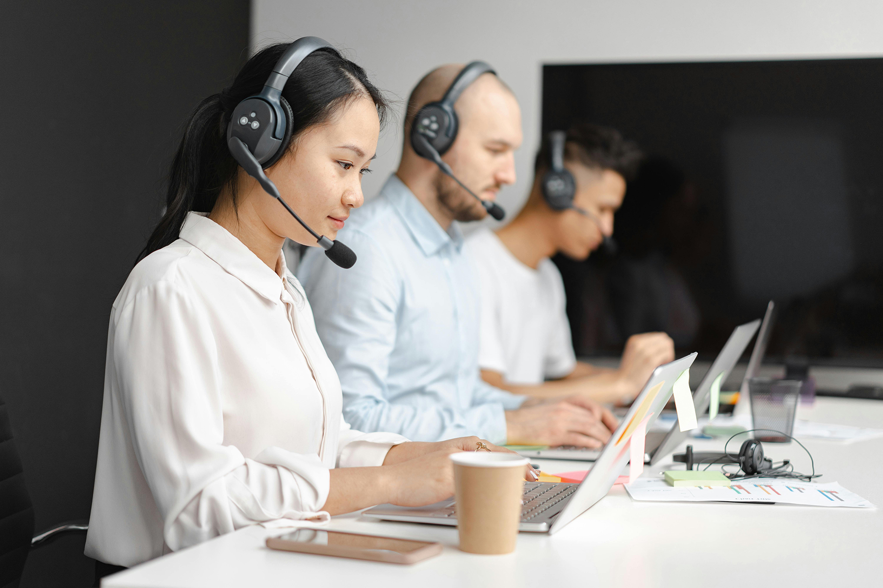 A busy, modern call center with diverse people wearing headphones, speaking into microphones, and working at their computers.