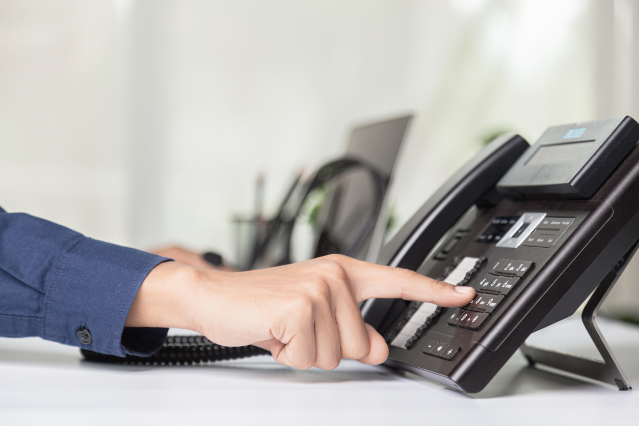 A staff member's hand pointing to and pressing a button on the office desk phone.